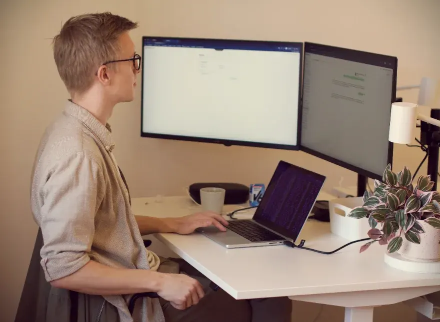 A PineGrove founder working at a desk with two monitors and a laptop